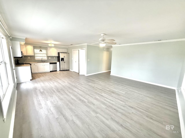 unfurnished living room featuring baseboards, ornamental molding, a sink, and light wood-style floors