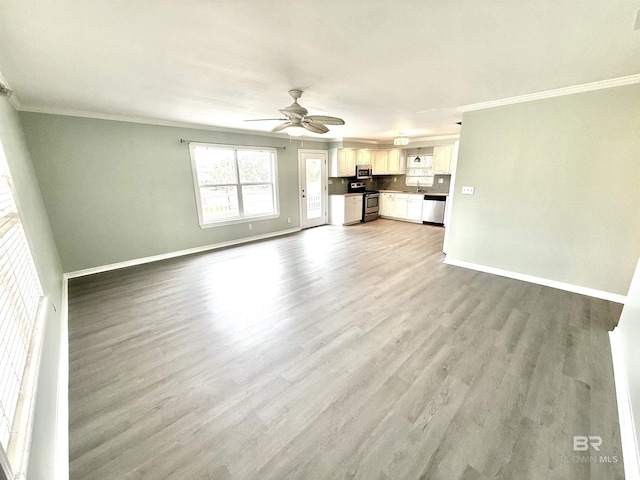 unfurnished living room with a sink, a ceiling fan, baseboards, light wood-type flooring, and crown molding