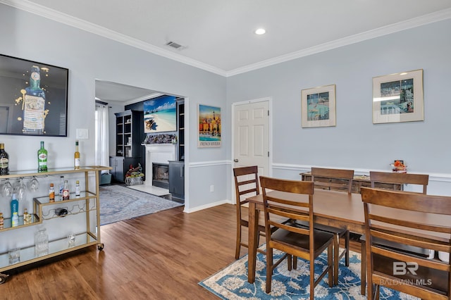 dining area featuring visible vents, baseboards, a fireplace with flush hearth, ornamental molding, and wood finished floors