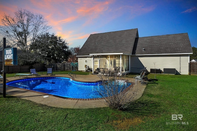 pool at dusk featuring a fenced backyard, a patio, a yard, and a sunroom