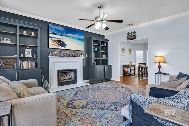 living room with built in features, wood finished floors, visible vents, a fireplace with flush hearth, and ornamental molding