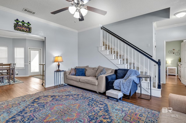 living area with stairway, wood finished floors, visible vents, and ornamental molding