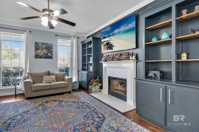 sitting room featuring built in features, wood finished floors, a textured ceiling, a tiled fireplace, and crown molding