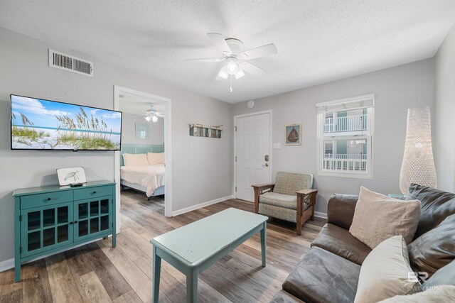 living room with a textured ceiling, wood-type flooring, and ceiling fan