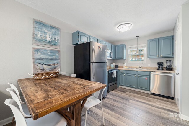 kitchen featuring appliances with stainless steel finishes, blue cabinets, light hardwood / wood-style flooring, decorative light fixtures, and sink