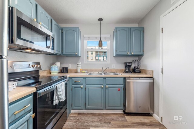 kitchen featuring sink, stainless steel appliances, decorative light fixtures, hardwood / wood-style floors, and blue cabinetry