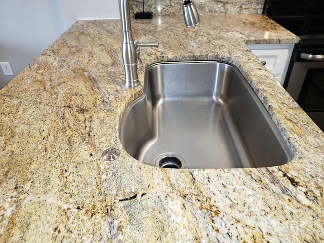 interior details with a sink, electric range, light stone counters, and white cabinets