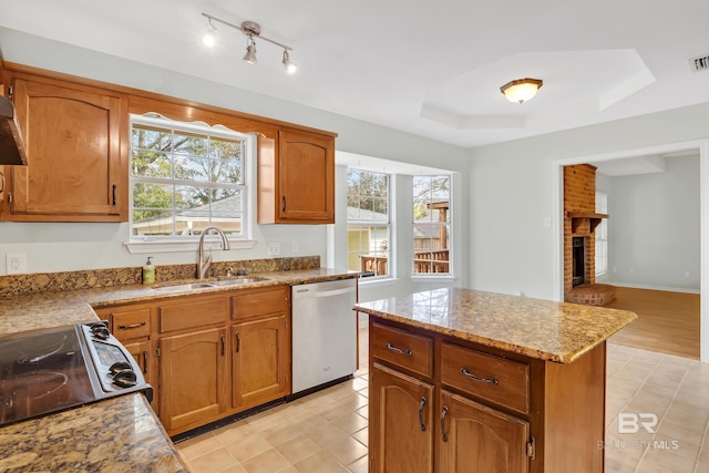 kitchen with brown cabinets, a sink, a tray ceiling, range with electric stovetop, and stainless steel dishwasher