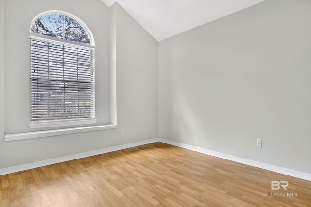 spare room with vaulted ceiling, baseboards, and light wood-type flooring