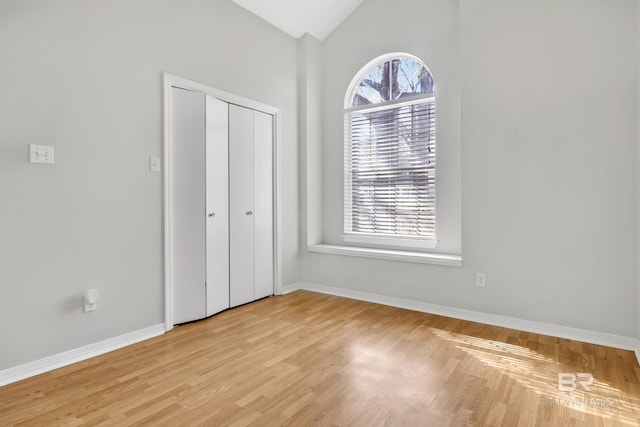 unfurnished bedroom with light wood finished floors, baseboards, and vaulted ceiling