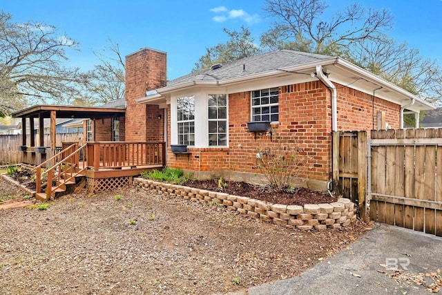 exterior space with a wooden deck, brick siding, a chimney, and fence