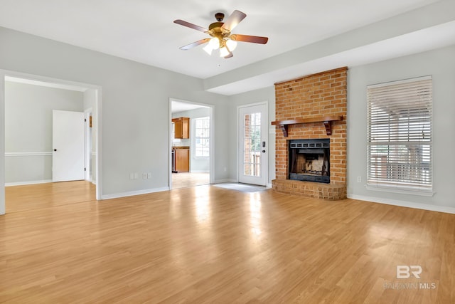 unfurnished living room featuring baseboards, a brick fireplace, ceiling fan, and light wood finished floors