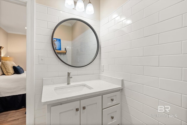 ensuite bathroom with ornamental molding, wood finished floors, ensuite bathroom, vanity, and tile walls