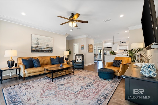 living area featuring baseboards, visible vents, crown molding, and wood finished floors