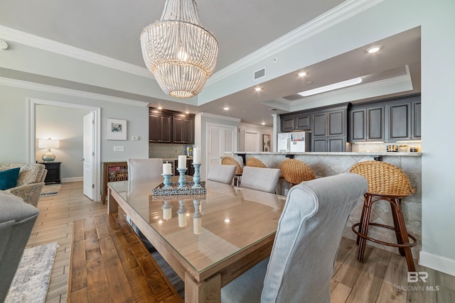 dining room with a raised ceiling, visible vents, light wood-style flooring, an inviting chandelier, and baseboards