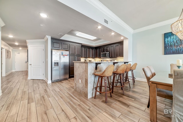 kitchen featuring stainless steel appliances, a breakfast bar, wood finish floors, a peninsula, and light stone countertops