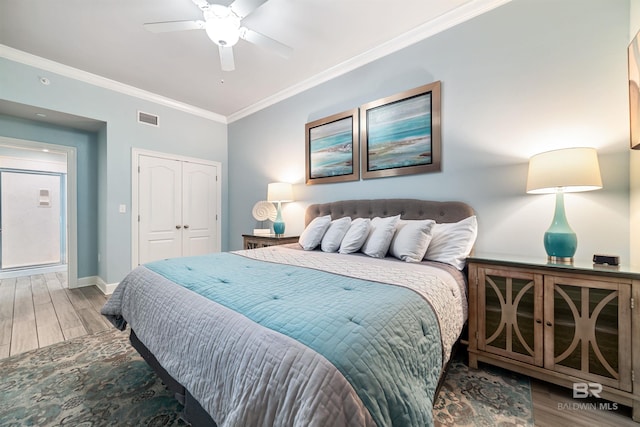 bedroom with crown molding, a closet, visible vents, wood finished floors, and baseboards