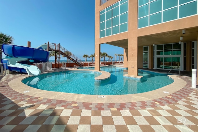 community pool featuring a water slide, a patio area, fence, and stairway