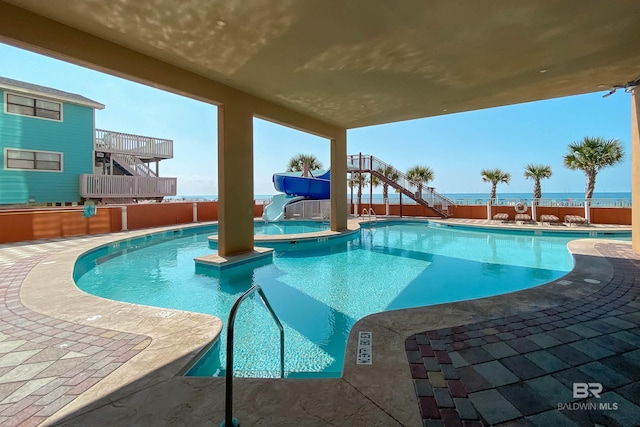 pool with a patio, a jacuzzi, stairway, fence, and a water slide