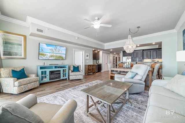 living room featuring ceiling fan, light wood-style flooring, visible vents, and crown molding