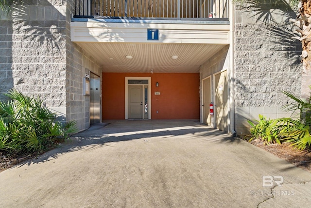 property entrance with elevator, a carport, and a balcony