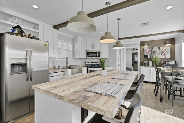 kitchen with light stone counters, stainless steel appliances, a kitchen island, white cabinets, and pendant lighting