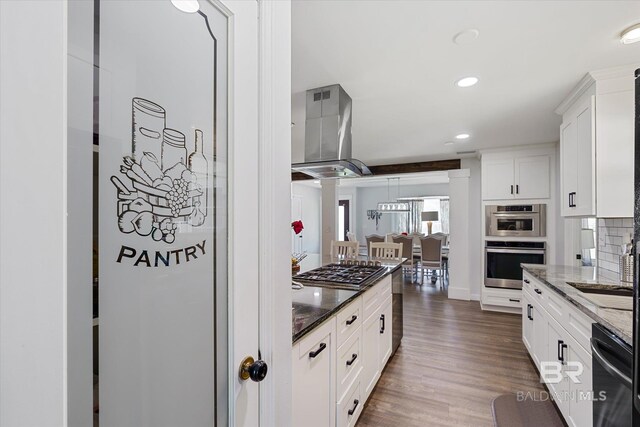 kitchen with white cabinetry, dark wood-type flooring, stainless steel appliances, range hood, and dark stone counters