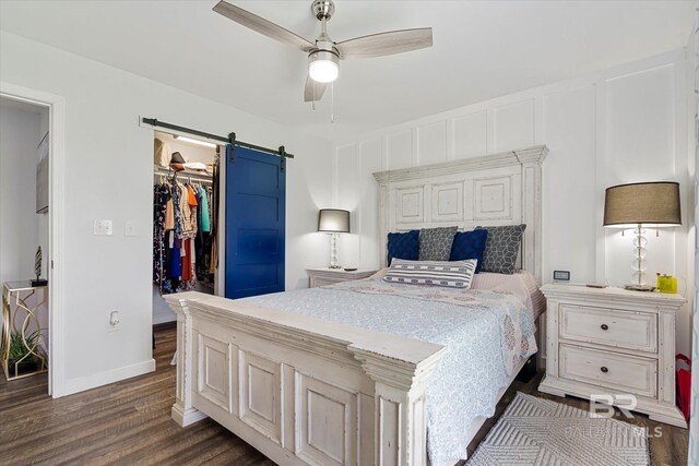 bedroom featuring ceiling fan, a walk in closet, a closet, dark hardwood / wood-style floors, and a barn door