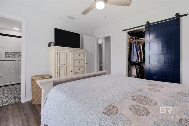 bedroom with a barn door, connected bathroom, dark hardwood / wood-style flooring, a closet, and ceiling fan