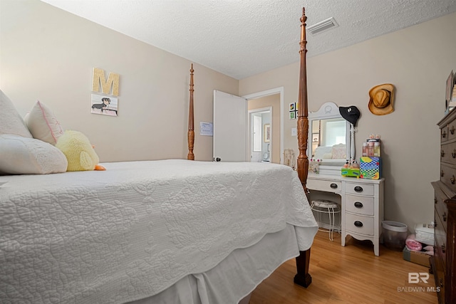 bedroom with wood finished floors, visible vents, and a textured ceiling