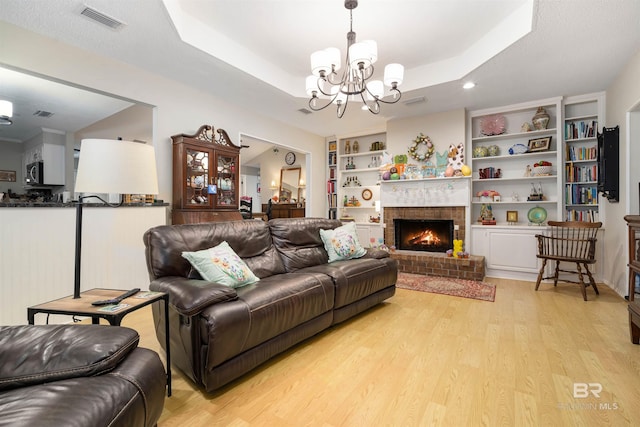 living area featuring visible vents, a chandelier, built in features, light wood-type flooring, and a tray ceiling