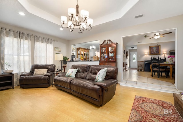 living area featuring ceiling fan with notable chandelier, a tray ceiling, visible vents, and light wood-type flooring