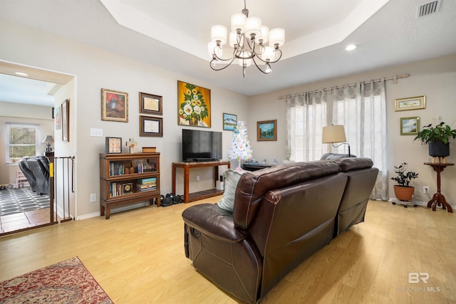 living room featuring visible vents, baseboards, light wood finished floors, a raised ceiling, and a chandelier