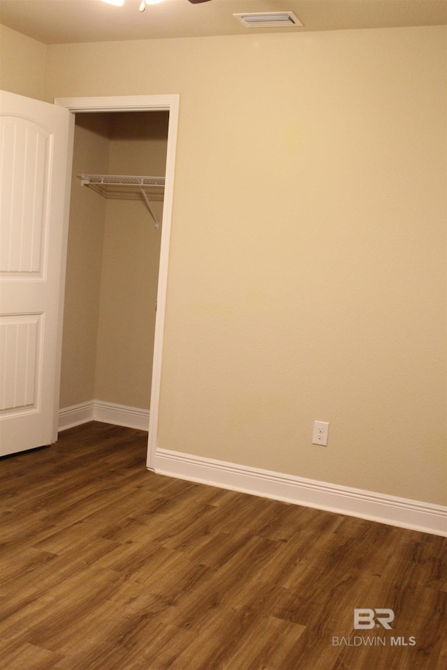 unfurnished bedroom with a closet, dark wood finished floors, visible vents, and baseboards