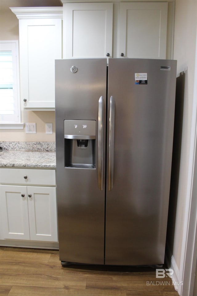 room details with light stone counters, light wood-style flooring, stainless steel fridge, and white cabinetry