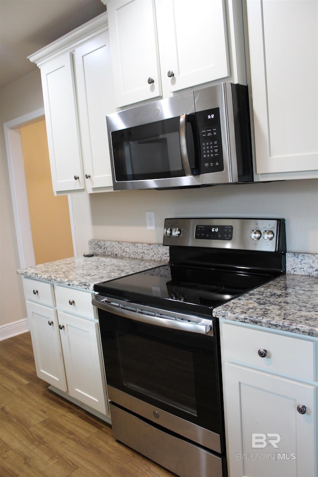 kitchen with light stone counters, wood finished floors, baseboards, white cabinets, and appliances with stainless steel finishes