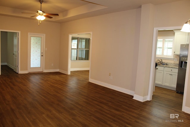 unfurnished living room featuring a sink, dark wood-type flooring, a raised ceiling, and baseboards