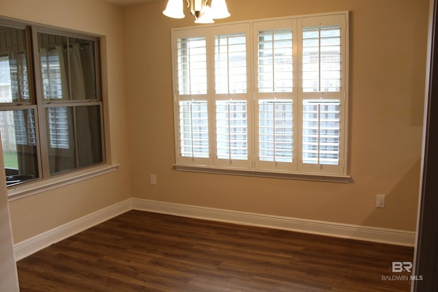 empty room featuring dark wood finished floors, baseboards, and an inviting chandelier