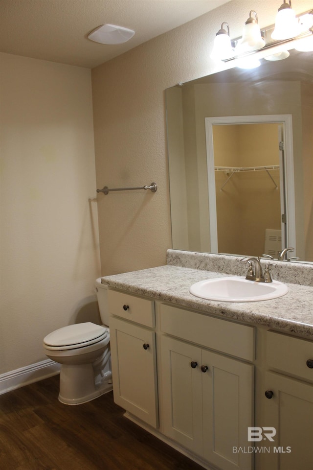 bathroom featuring vanity, wood finished floors, toilet, and a walk in closet