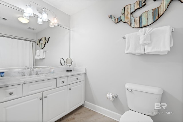 bathroom with visible vents, toilet, vanity, wood finished floors, and baseboards