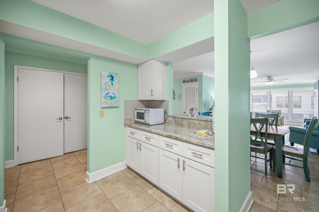 kitchen with ceiling fan, light stone counters, white cabinetry, and light tile patterned flooring