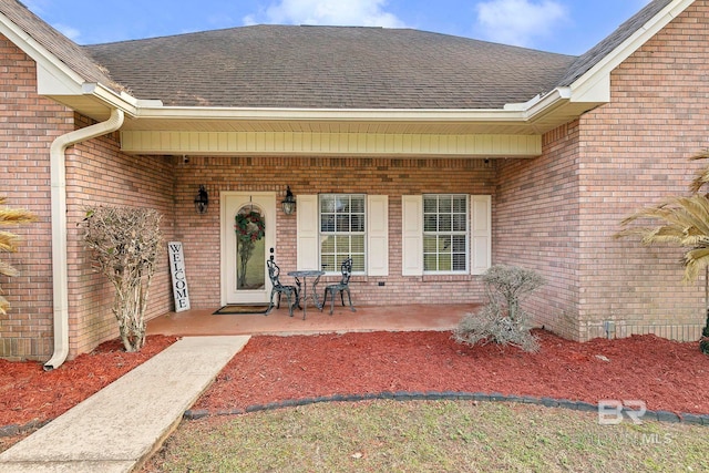 doorway to property with covered porch, brick siding, and roof with shingles