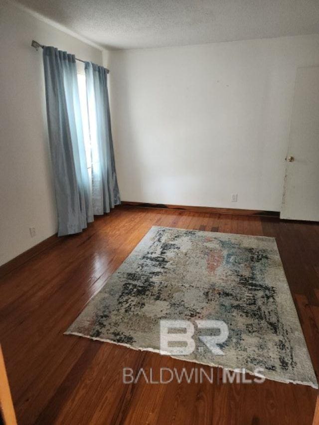 unfurnished room with a textured ceiling, wood finished floors, and baseboards