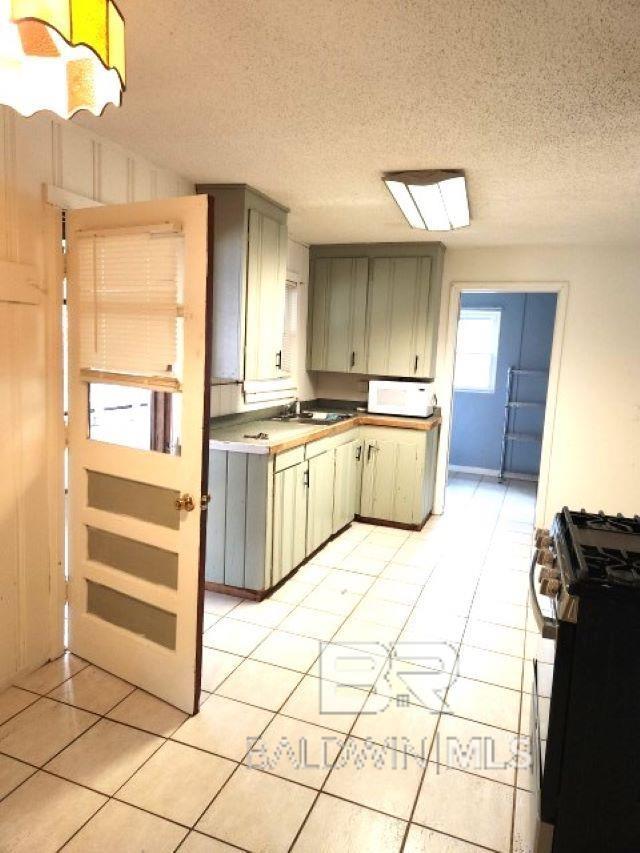 kitchen with stainless steel gas stove, white microwave, a textured ceiling, light countertops, and a sink
