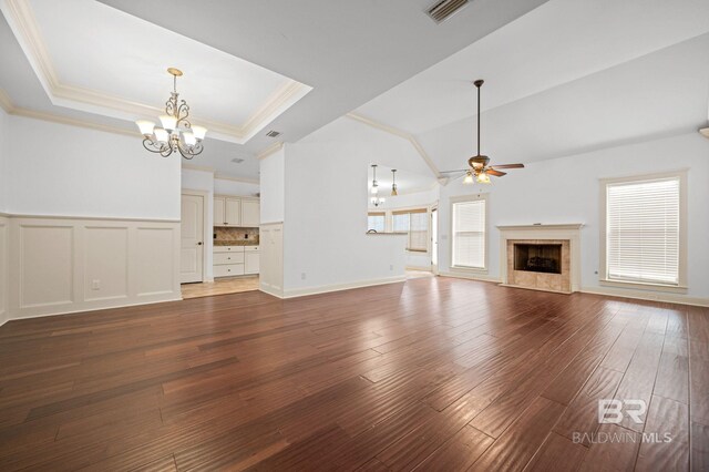 unfurnished living room with crown molding, a tray ceiling, a fireplace, ceiling fan with notable chandelier, and hardwood / wood-style flooring