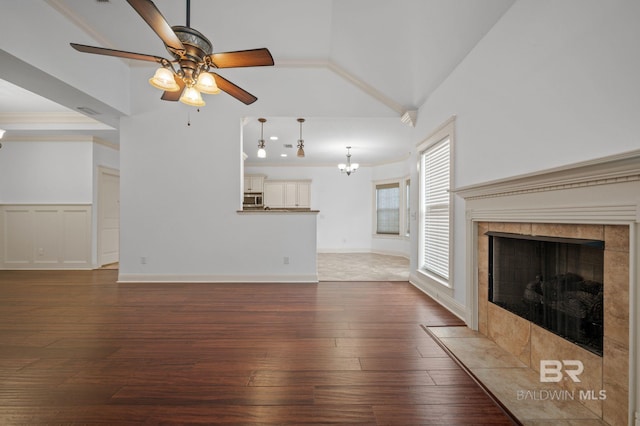 unfurnished living room with hardwood / wood-style floors, lofted ceiling, a tile fireplace, ceiling fan with notable chandelier, and crown molding