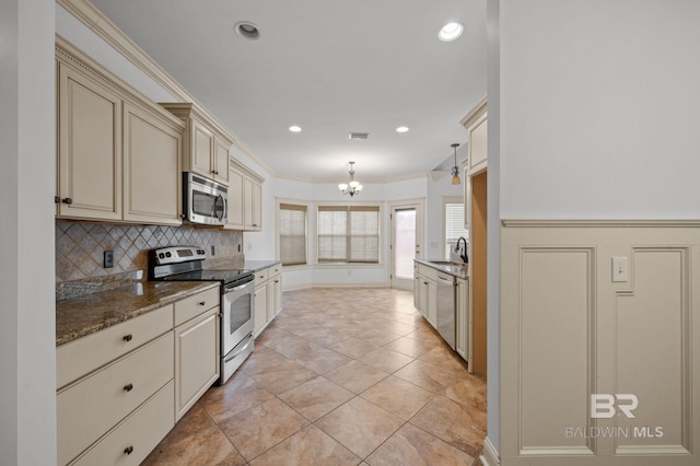 kitchen with ornamental molding, stainless steel appliances, sink, cream cabinetry, and hanging light fixtures