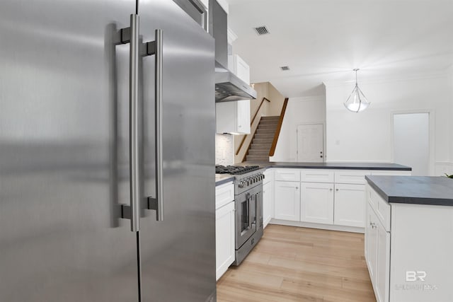 4340 Hamilton Oaks Ln, Mobile, AL 36695 - kitchen with premium appliances, dark countertops, wall chimney exhaust hood, a peninsula, and light wood-style floors