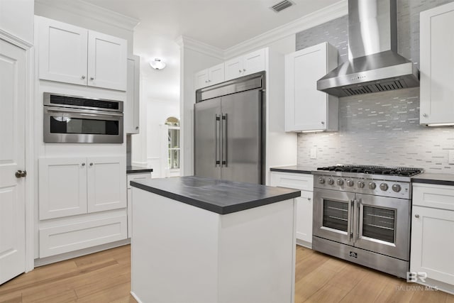 4340 Hamilton Oaks Ln, Mobile, AL 36695 - kitchen with wall chimney exhaust hood, high end appliances, dark countertops, light wood-type flooring, and crown molding