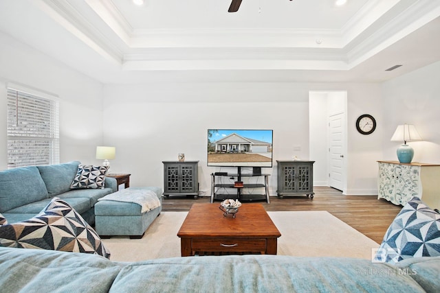 living room with crown molding, a tray ceiling, wood-type flooring, and a healthy amount of sunlight